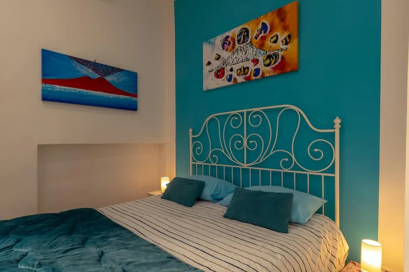 Il letto matrimoniale in ferro battuto sulla parete turchese, con le lampade accese sui comodini.