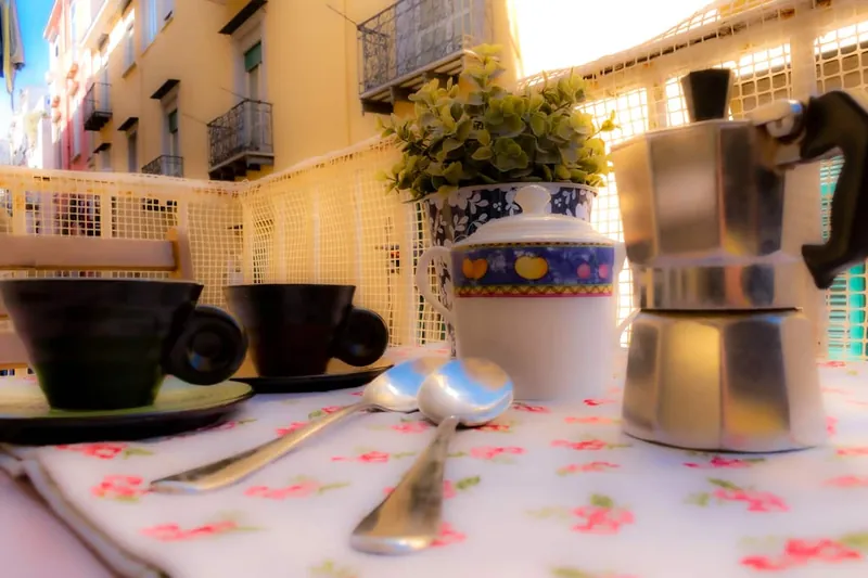 La moka e due tazzine sulla tovaglia a fiori, con il vicolo sullo sfondo.